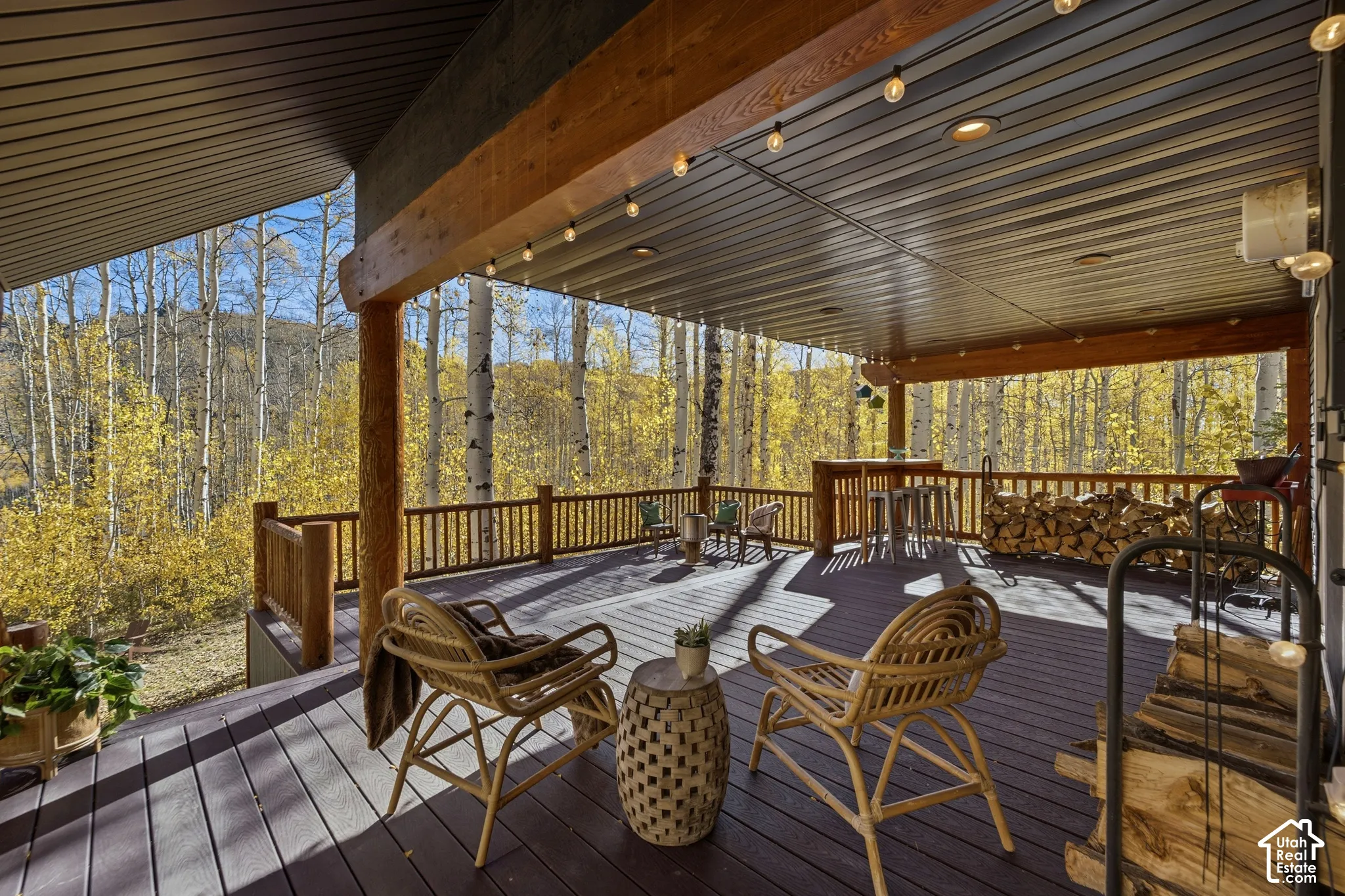 Covered exterior deck featuring composite decking, exposed timber support beams, and a wood railing overlooking a grove of aspen trees