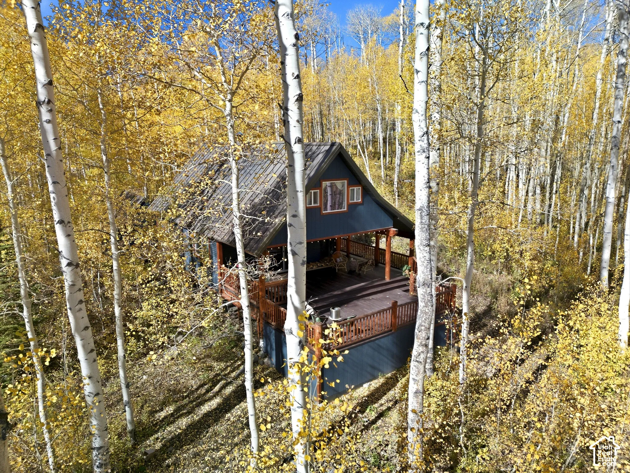 Gabled cabin exterior featuring a tiered wood deck, metal roofing, log-style timber accents, and surrounding aspen woodland
