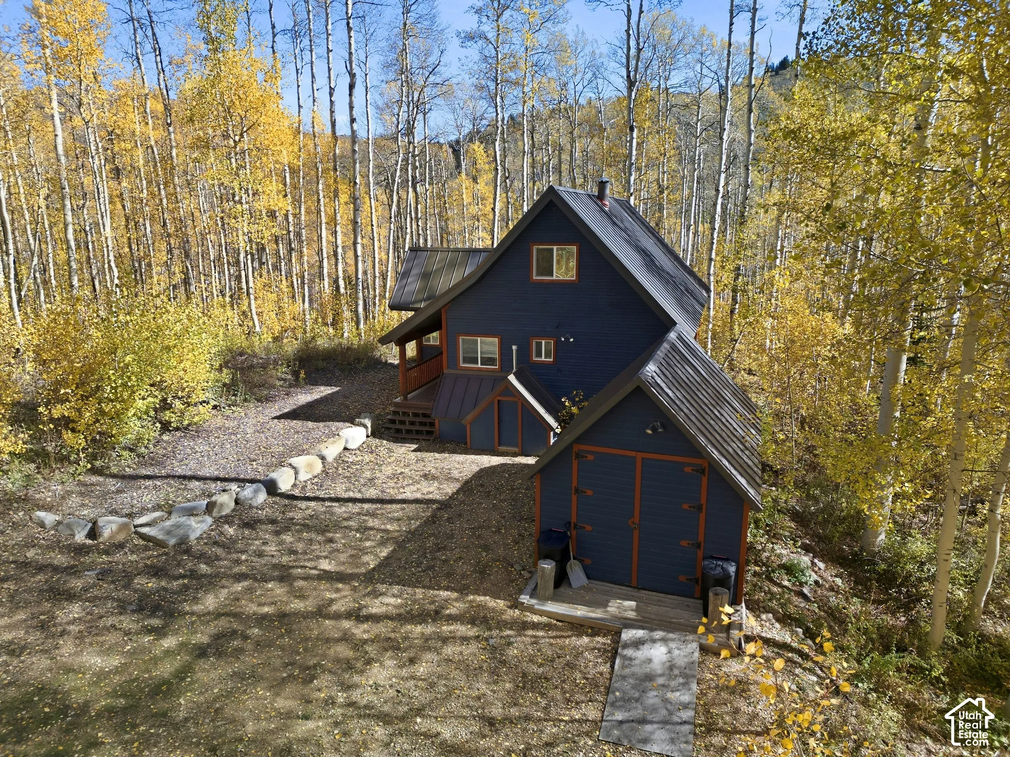 Multi-level residence featuring dark wood-lap siding, standing-seam metal roofing, detached storage structure, and a boulder-lined landscaping feature surrounded by an aspen grove