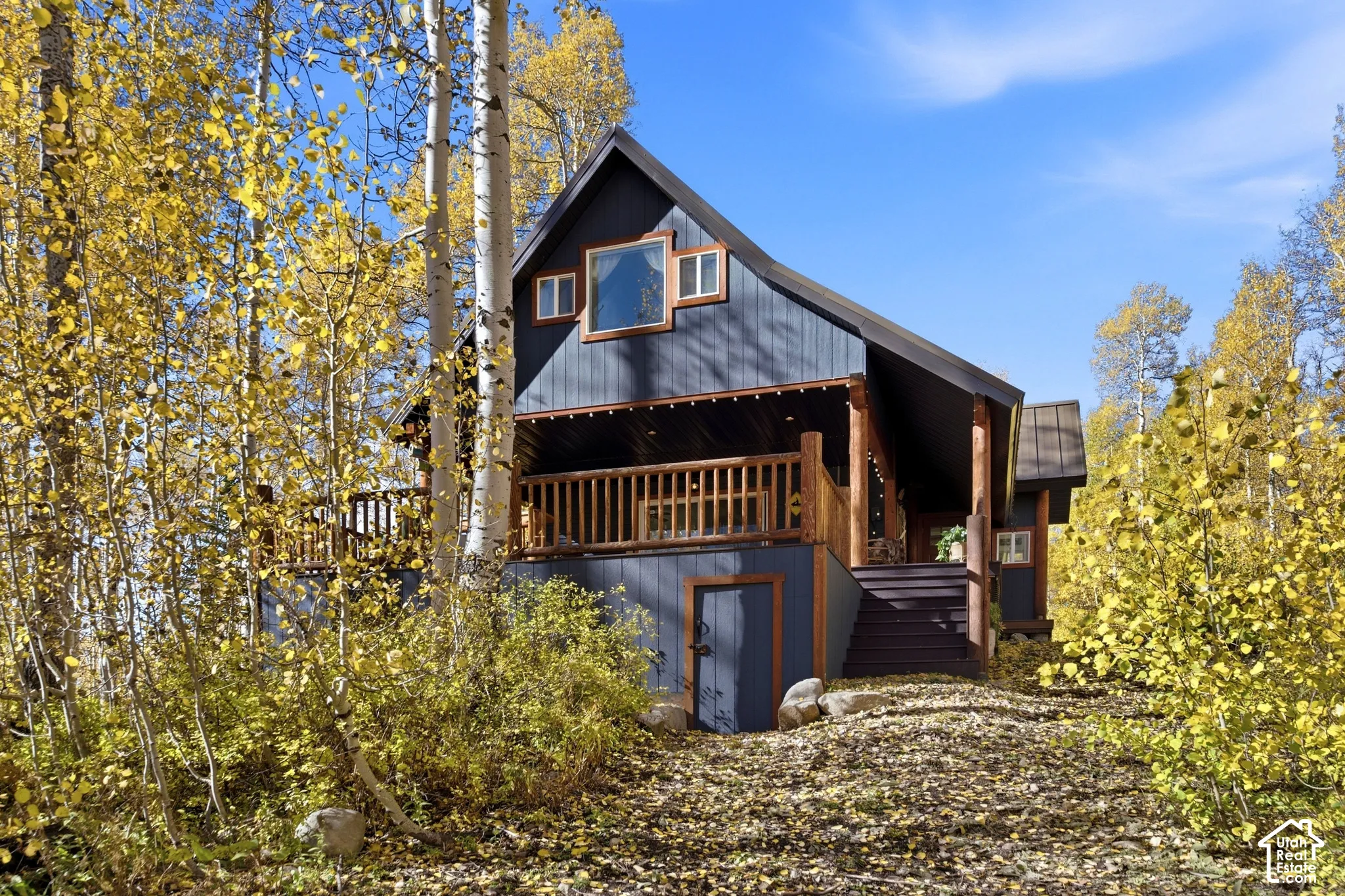 Exterior featuring board and batten siding, wraparound wood deck with railing, metal roof, and integrated ground-level storage access