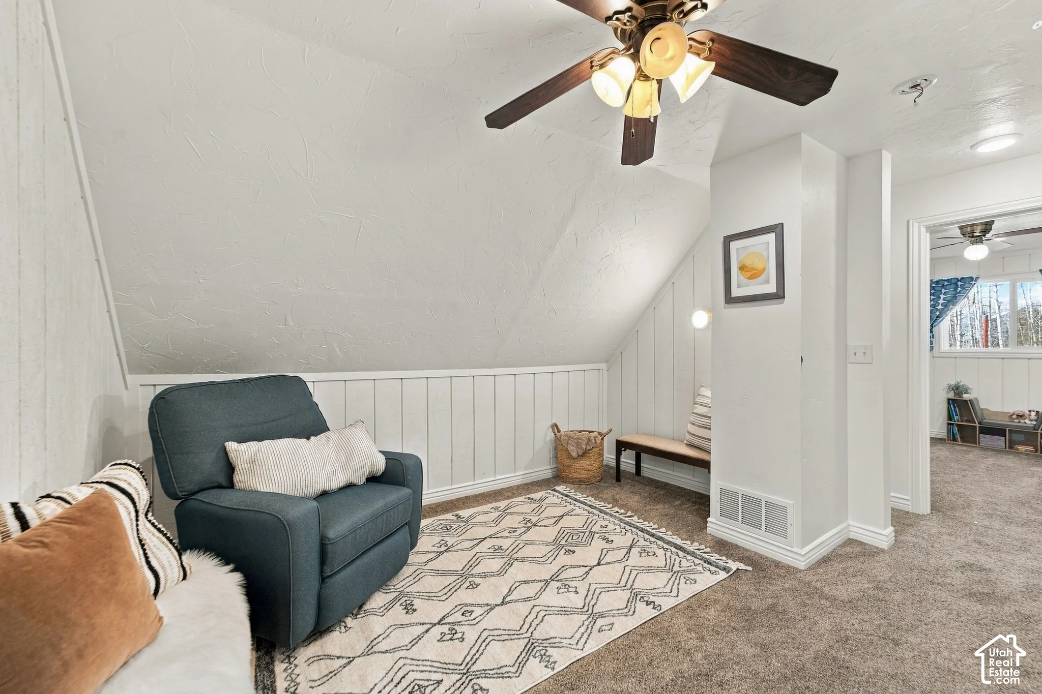 Vaulted ceiling, vertical plank wall paneling, ceiling fan with integrated lighting, and neutral carpeting