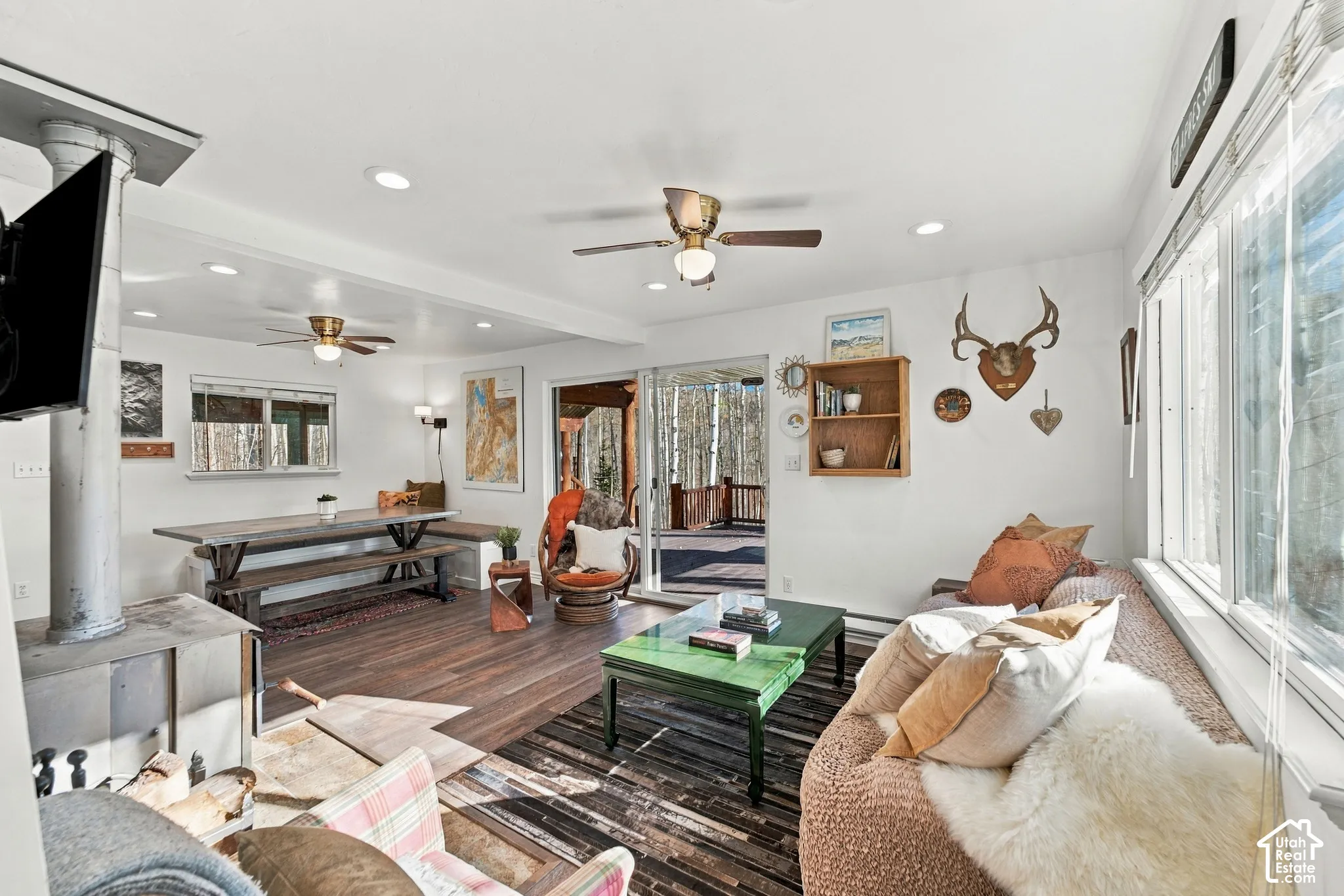 Open-concept living space featuring wood-finish flooring, a metal wood-burning stove, dual ceiling fans, recessed lighting, and sliding glass doors