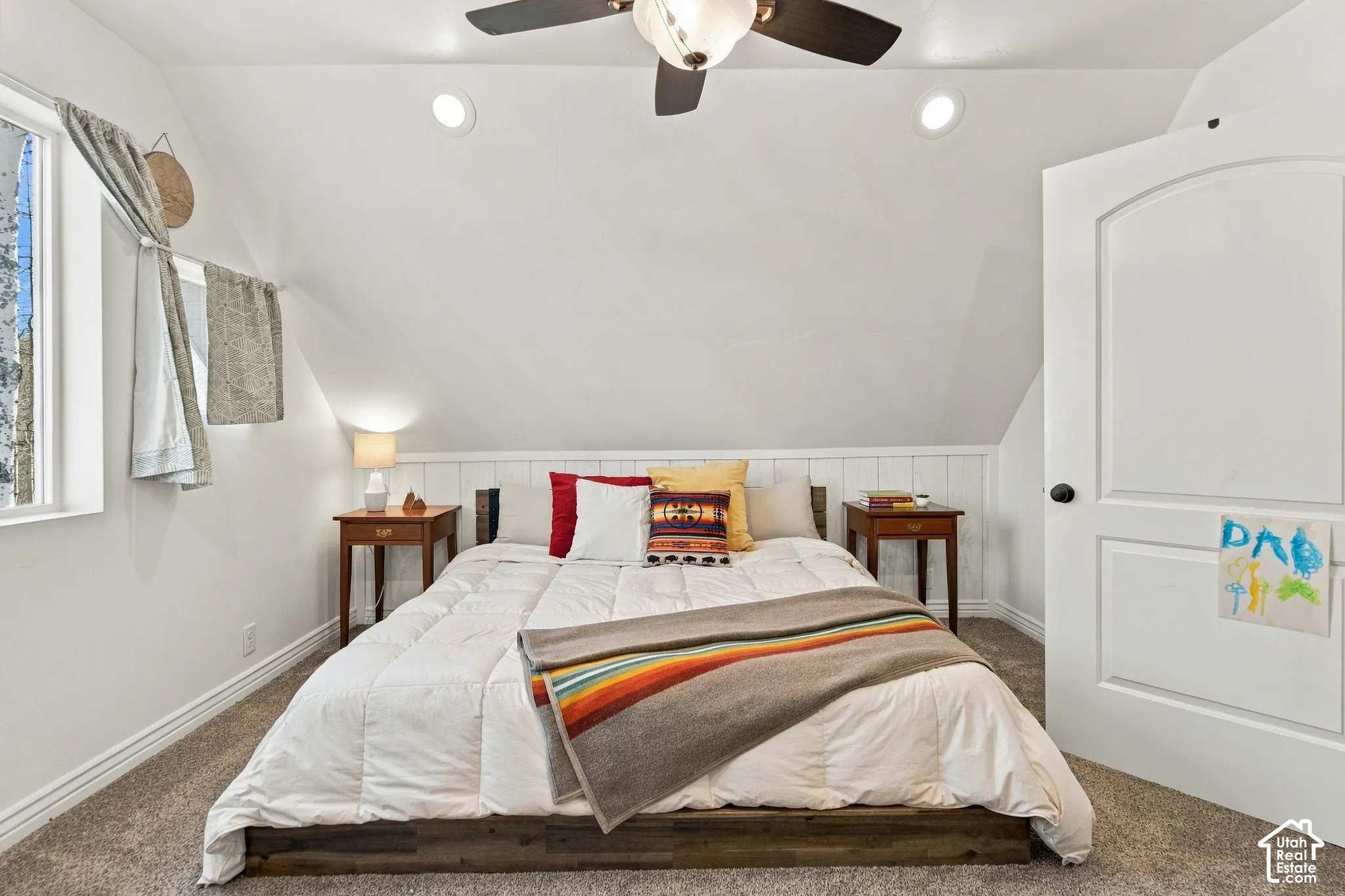 Room featuring vaulted ceilings, vertical shiplap wall detail, carpeted flooring, a ceiling fan with integrated lighting, and a multi-panel interior door