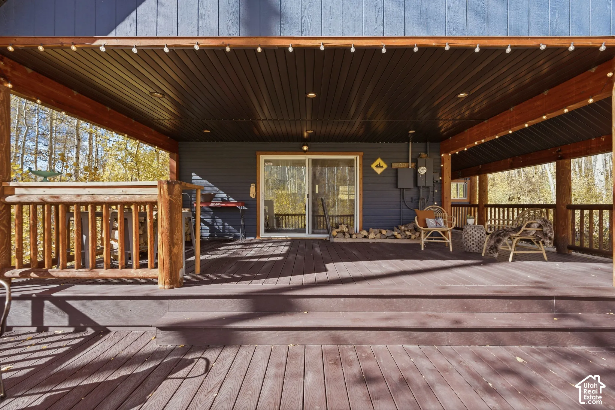 Covered wooden deck featuring natural log post supports, vertical board siding, recessed ceiling lighting, and sliding glass door entry