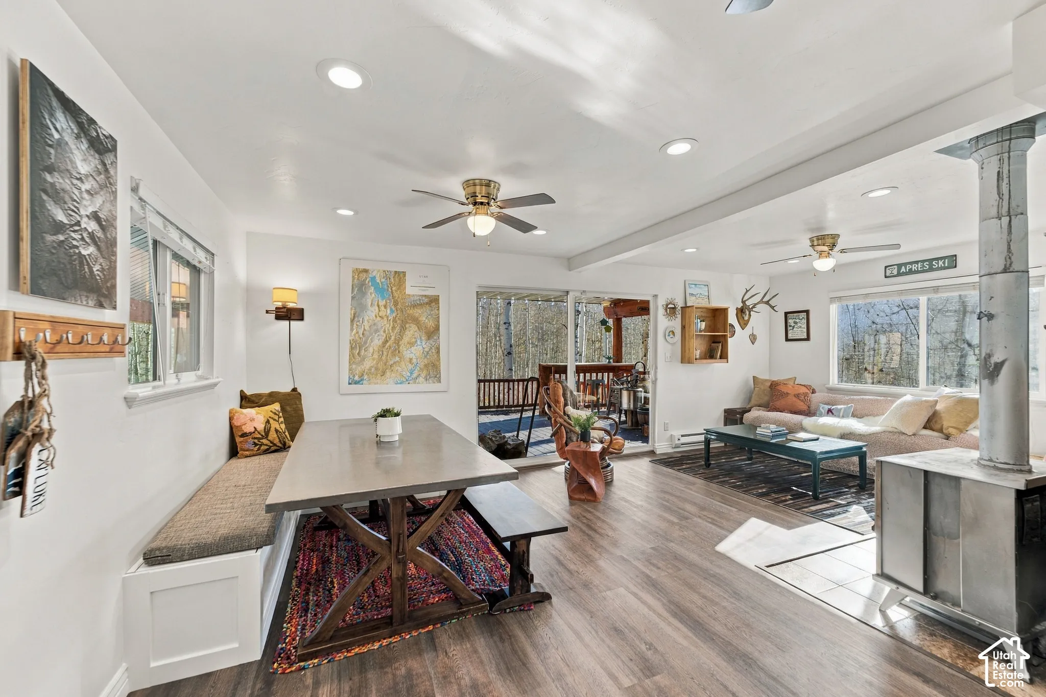 Open-concept living space featuring wood-finish flooring, recessed lighting, ceiling fans, a built-in bench seat, and a metal-encased wood-burning stove on a tile hearth