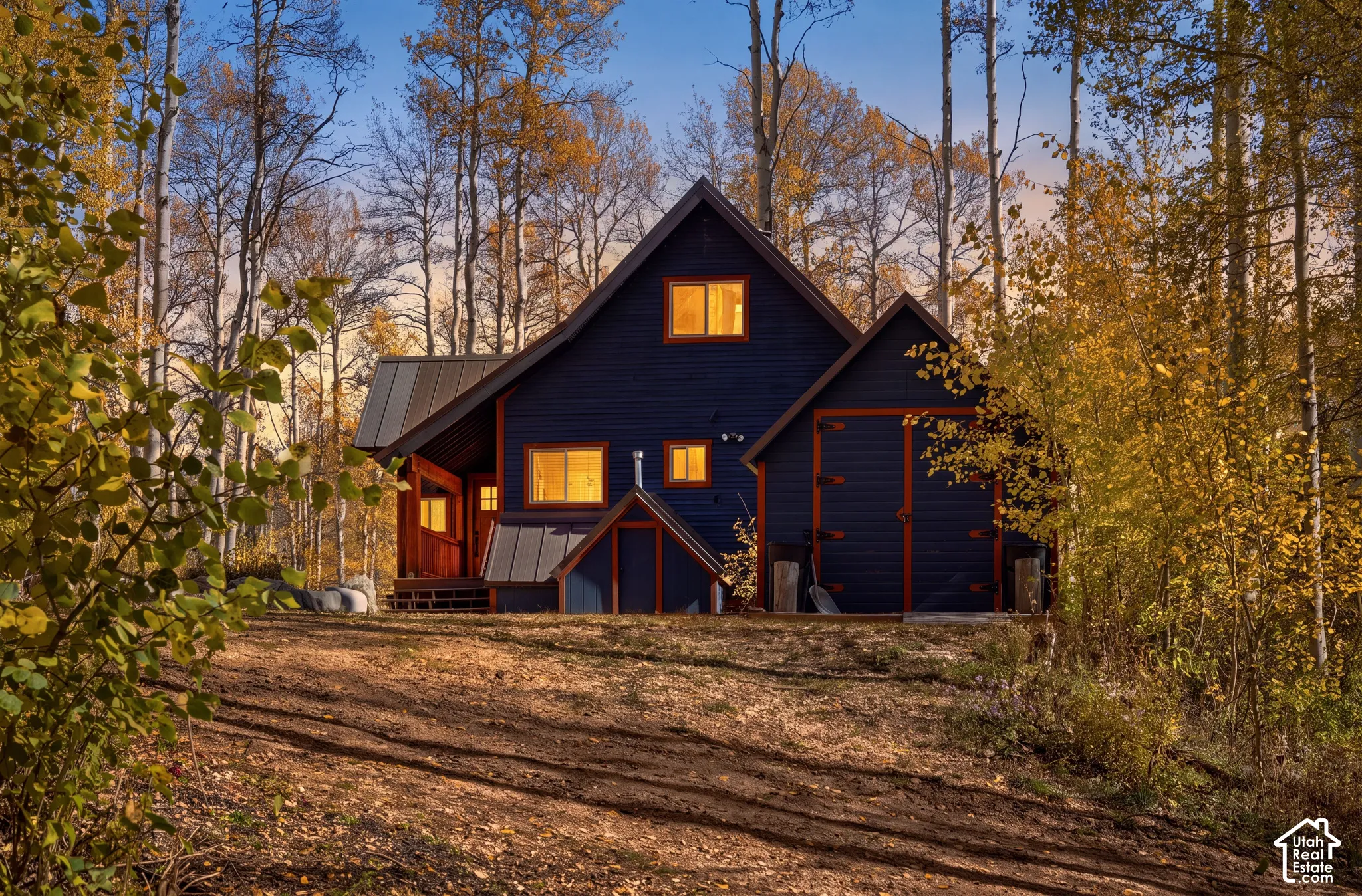 Gable-roofed residence featuring dark horizontal lap siding, metal roofing, an attached garage with double doors, and a covered entry deck