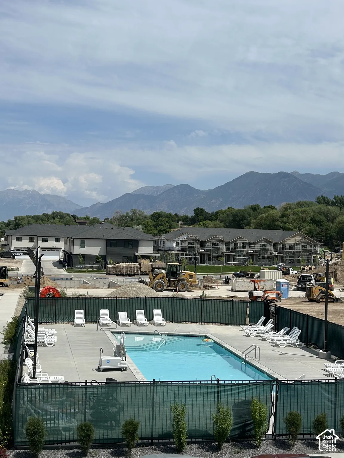 Outdoor swimming pool with concrete decking, perimeter metal fencing, and mountain backdrop