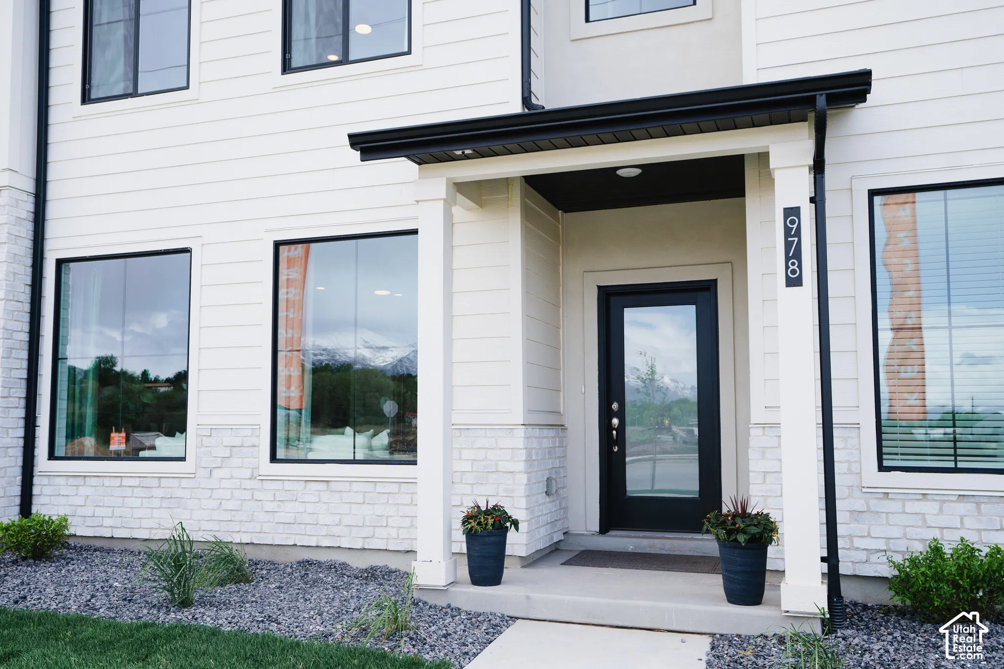 Exterior facade featuring white horizontal siding, a stone veneer base, black window frames, and a covered entryway with a glass-paneled door