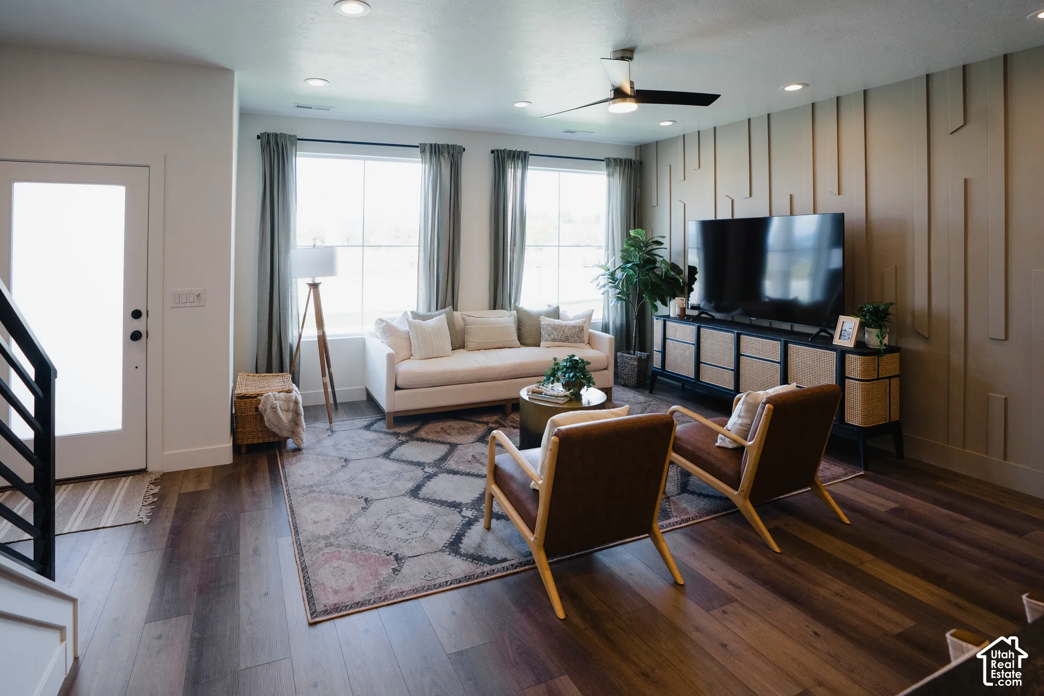 Living area featuring wood-finish flooring, accent wall with vertical millwork, recessed lighting, ceiling fan, and large windows