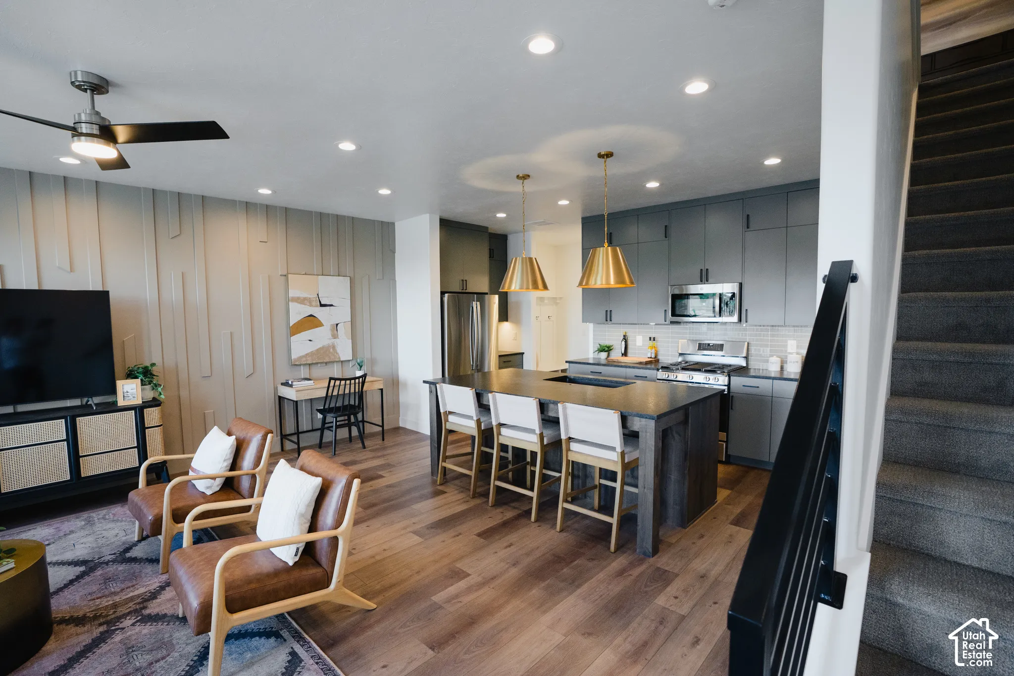 Kitchen featuring grey shaker-style cabinetry, a stone-topped island with integrated seating, recessed ceiling lighting, wood-finish flooring, and a decorative vertical slat wall feature