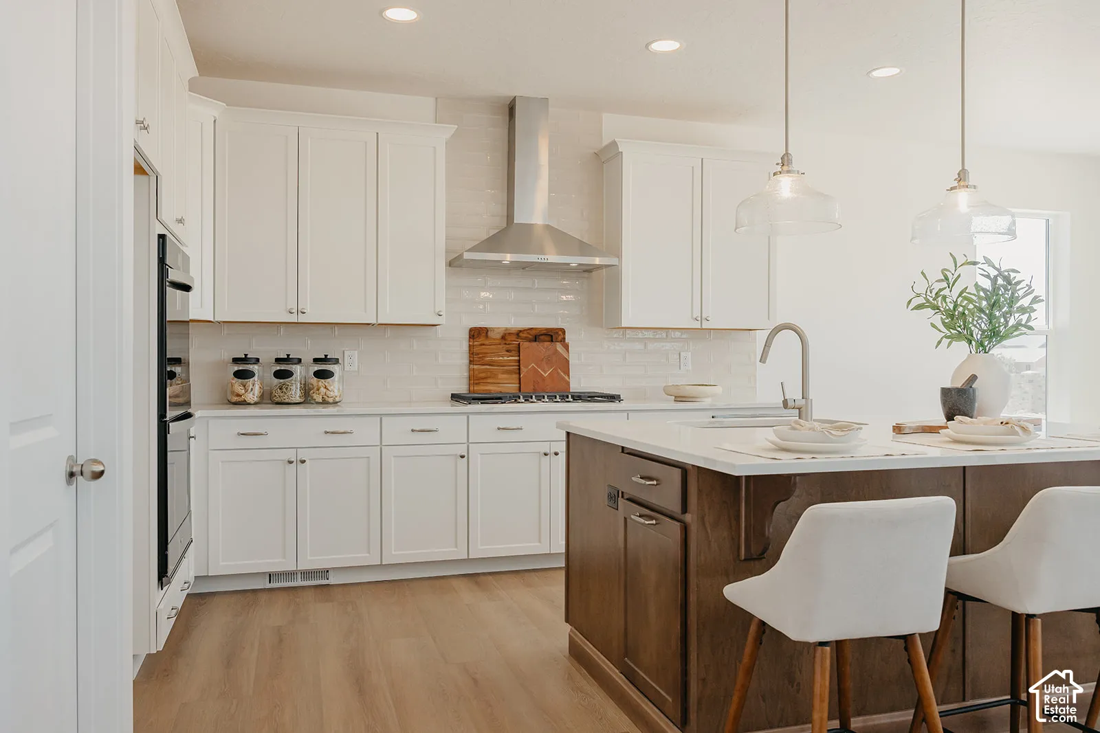 Kitchen featuring white cabinetry, wood-finish flooring, a stainless steel range hood, stone countertops, and a kitchen island with built-in cabinetry