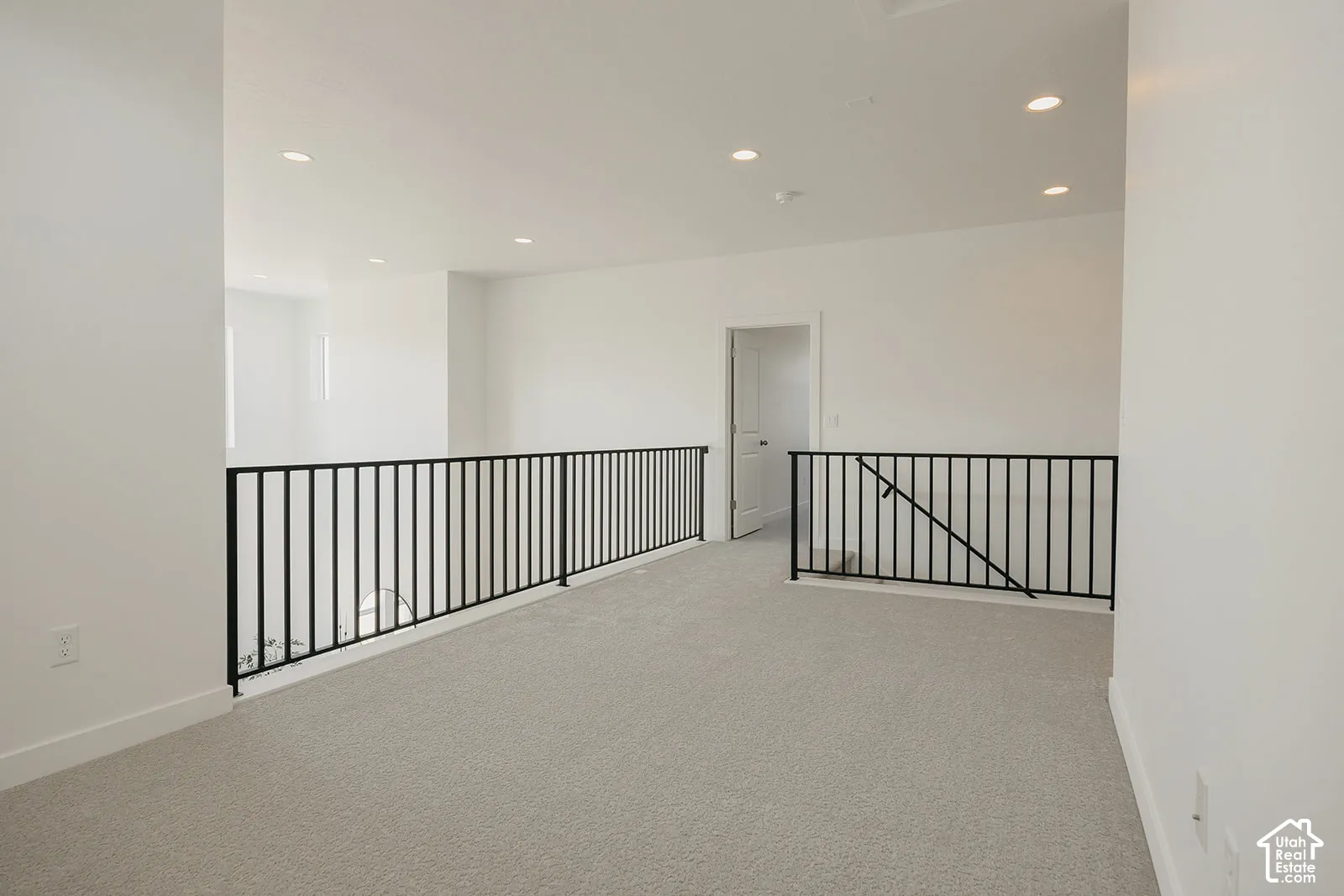 Open floor area featuring neutral carpeting, recessed ceiling lighting, and black metal handrail balusters
