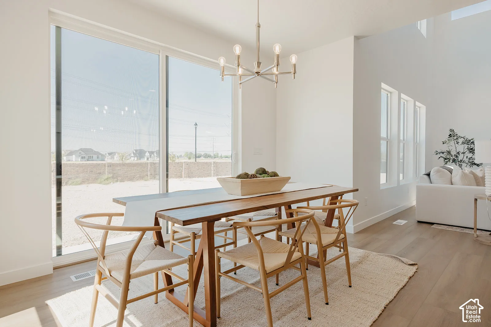 Tall ceilings with expansive sliding glass doors, neutral wood-finish flooring, and a modern multi-arm chandelier