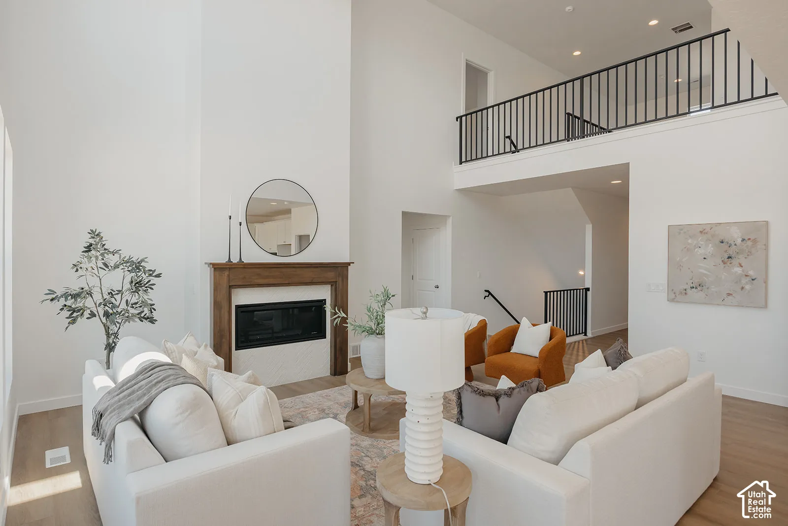Double-height ceiling, fireplace with a wood mantel, open mezzanine with black metal railing, and wood-finish flooring