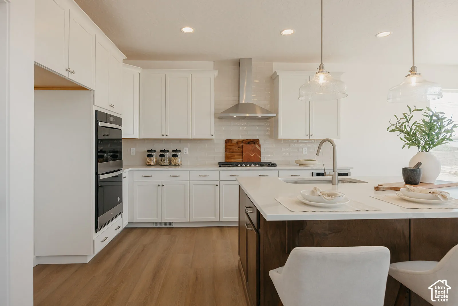 Kitchen featuring white shaker-style cabinetry, quartz countertops, a central island with a contrasting dark wood-finish base, stainless steel wall oven, and pendant lighting