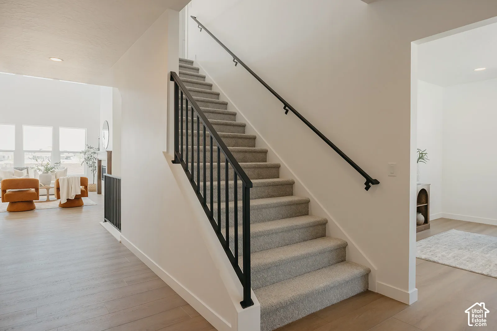 Staircase featuring carpeted treads, a black metal balustrade, and a matching wall-mounted handrail, complemented by wood-finish flooring