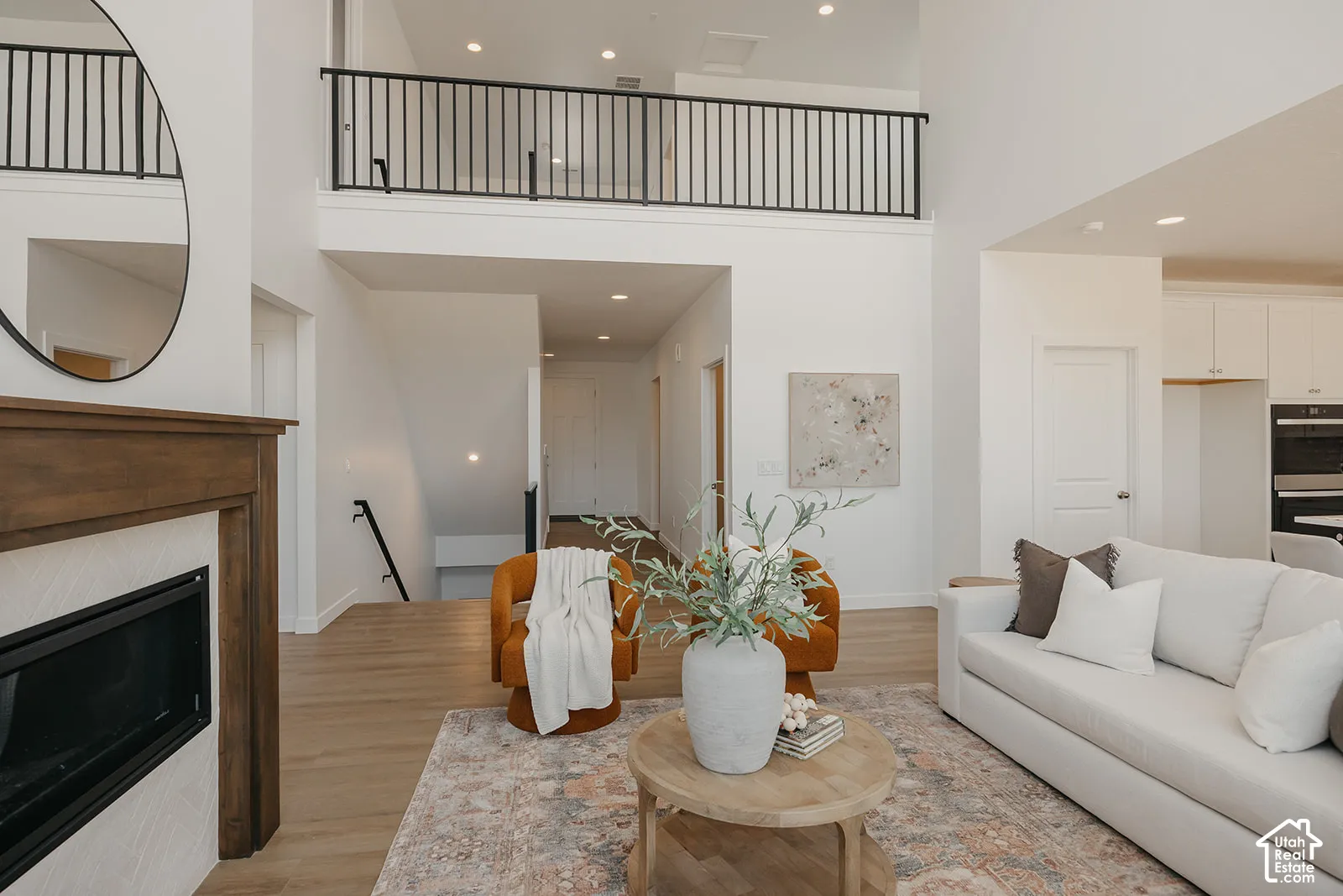 Double-height ceiling, fireplace with wood mantel and herringbone tile surround, metal-railing overlook, and wood-finish flooring