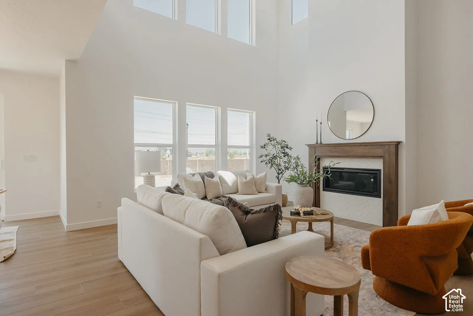 Double-height ceilings featuring expansive windows, wood-finish flooring, and a fireplace with a wood mantel and herringbone-patterned tile surround