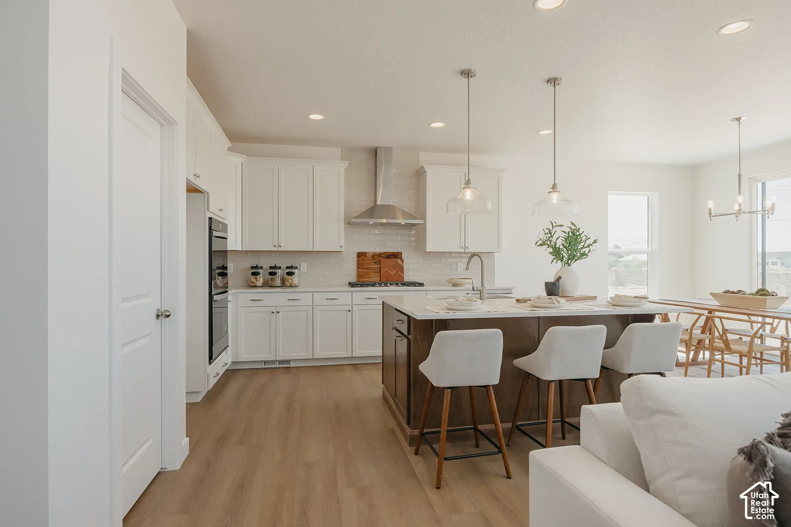 Kitchen featuring white cabinetry, wood-finish flooring, a central island with a stone-finish countertop, a stainless steel chimney-style range hood, and recessed lighting