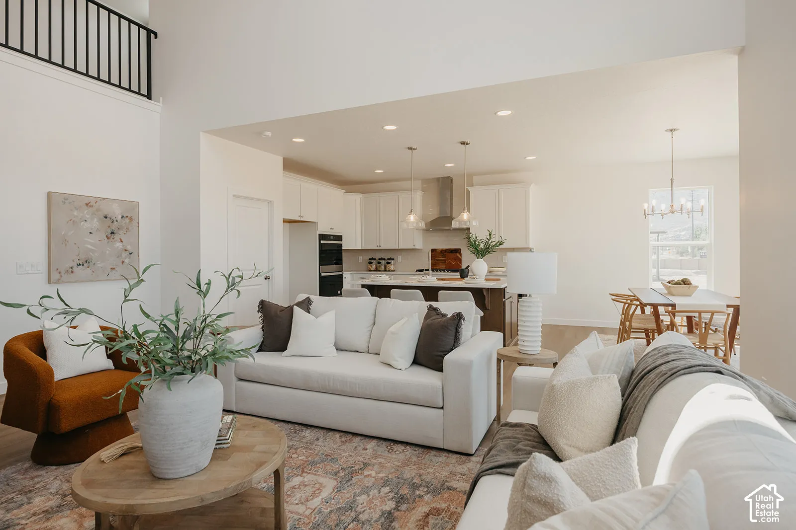 Open-concept interior featuring vaulted ceilings, a kitchen with white cabinetry and a central island, recessed lighting, and a metal stair railing