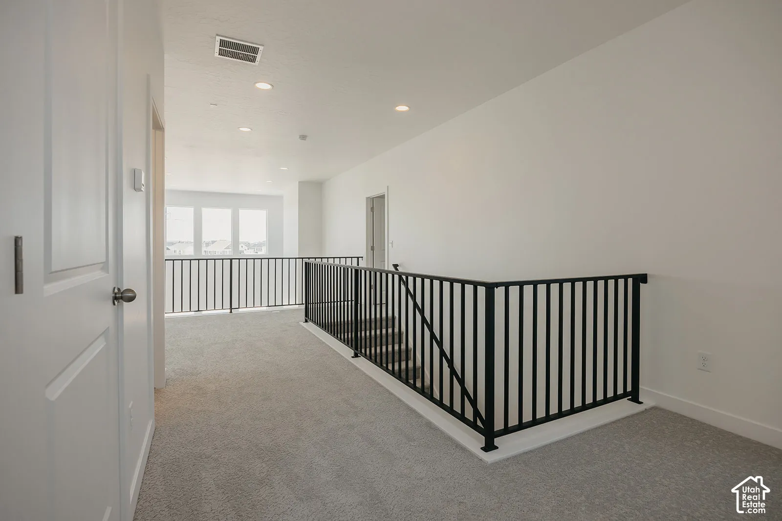 Open-concept landing featuring neutral wall-to-wall carpeting, black metal baluster railings, and recessed ceiling lighting