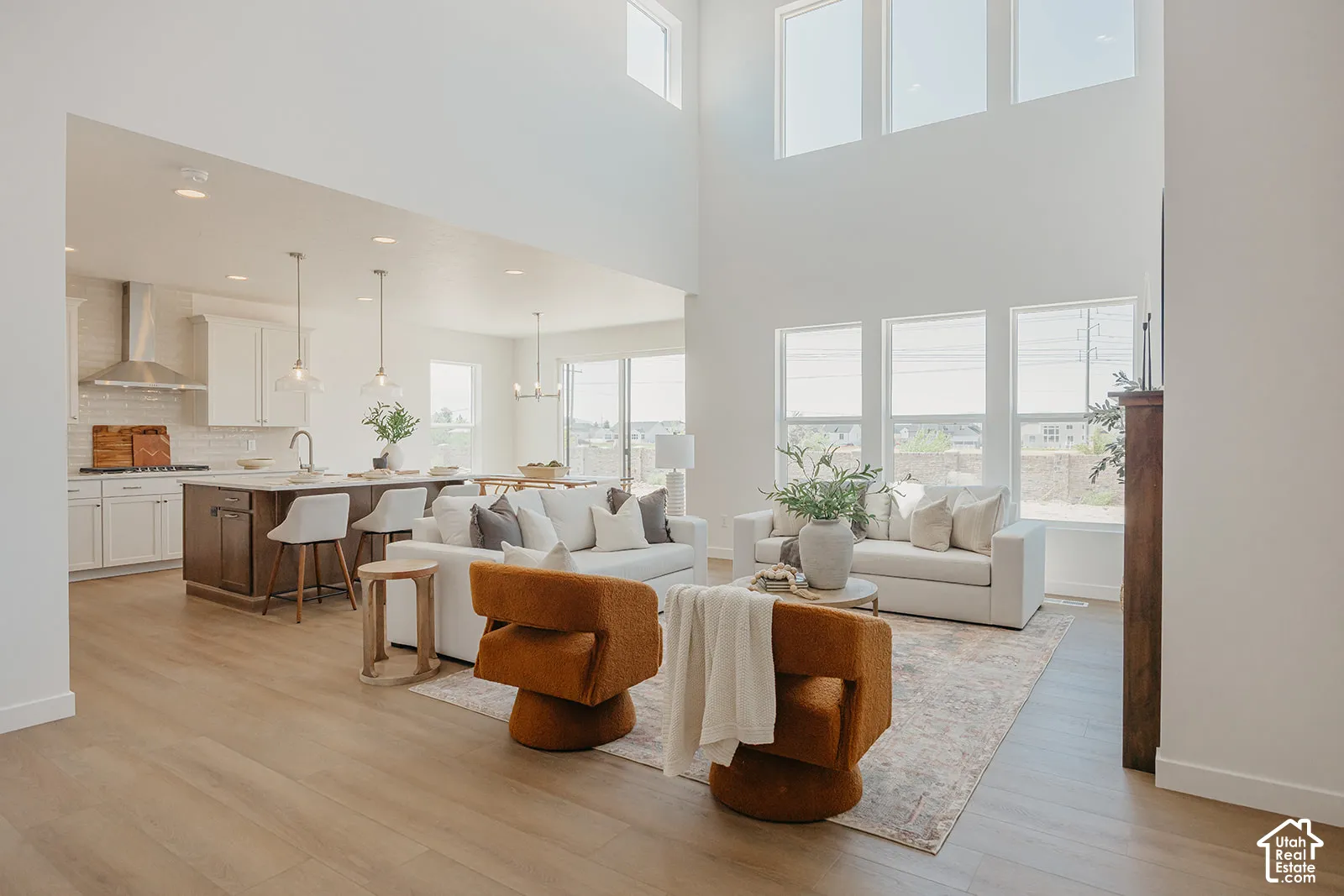 Open-concept interior featuring double-height ceilings, expansive multi-pane windows, wood-finish flooring, and a kitchen equipped with a center island and stainless steel vent hood