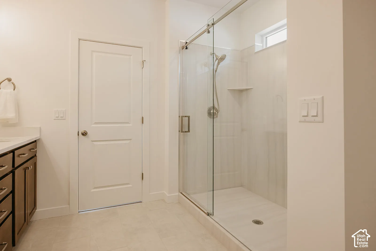 Walk-in shower featuring a glass enclosure, rainfall showerhead, and integrated shelving, complemented by dark wood-finish cabinetry and a solid-surface countertop