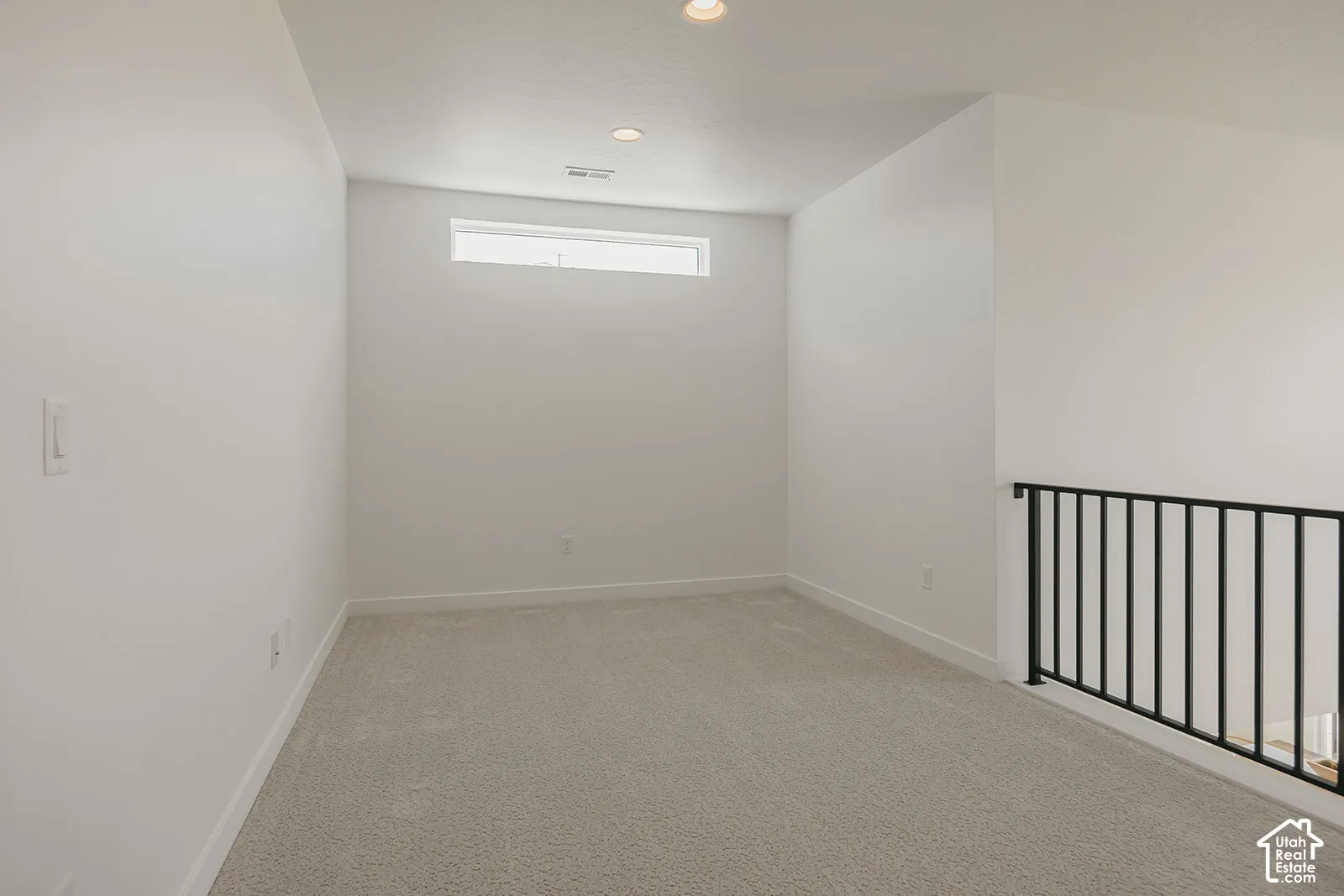 Interior space featuring neutral carpeting, recessed ceiling lighting, a horizontal clerestory window, and a black metal railing