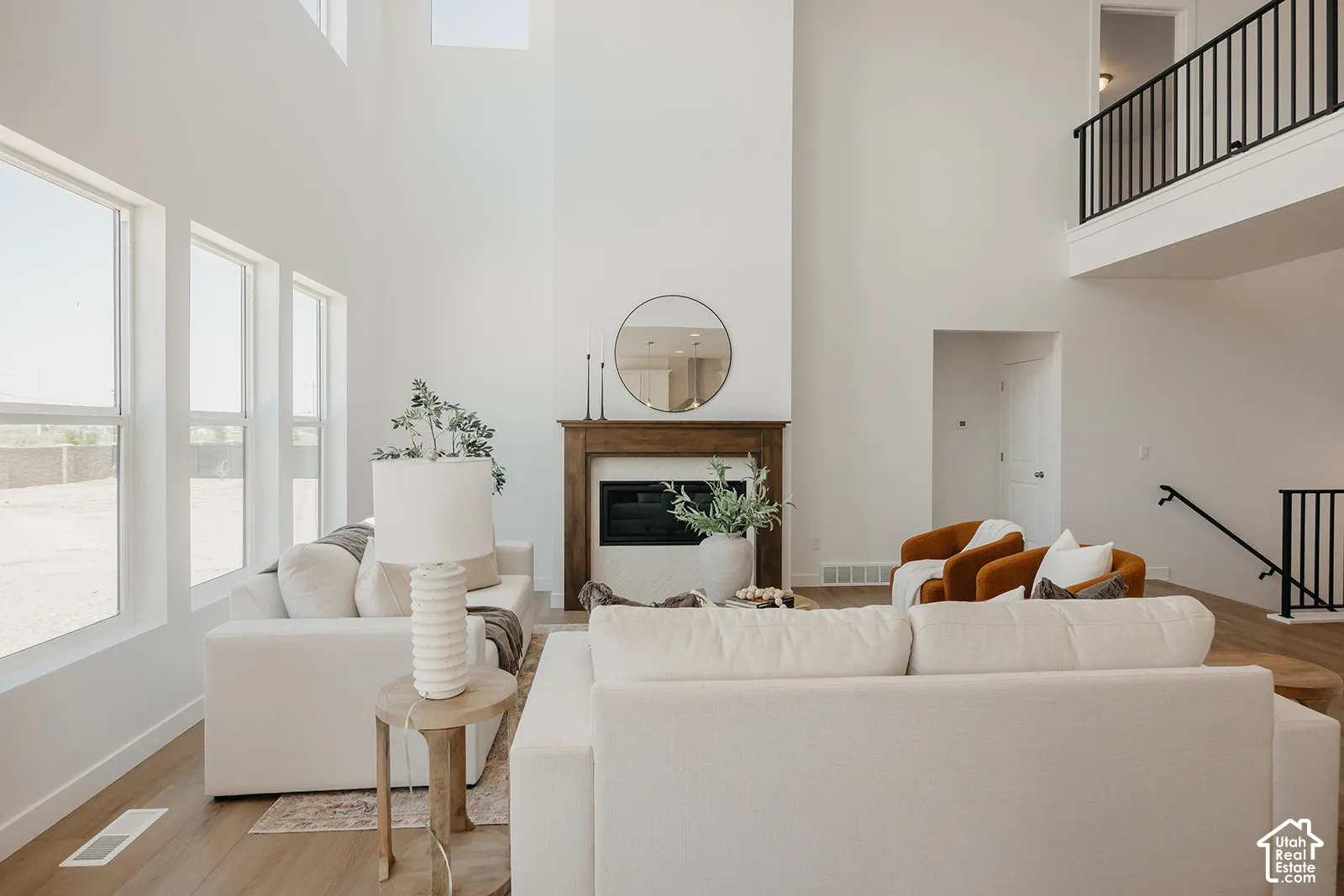 Two-story vaulted ceiling with expansive floor-to-ceiling windows, gas fireplace featuring a wood mantel, wood-finish flooring, and a metal-railed mezzanine