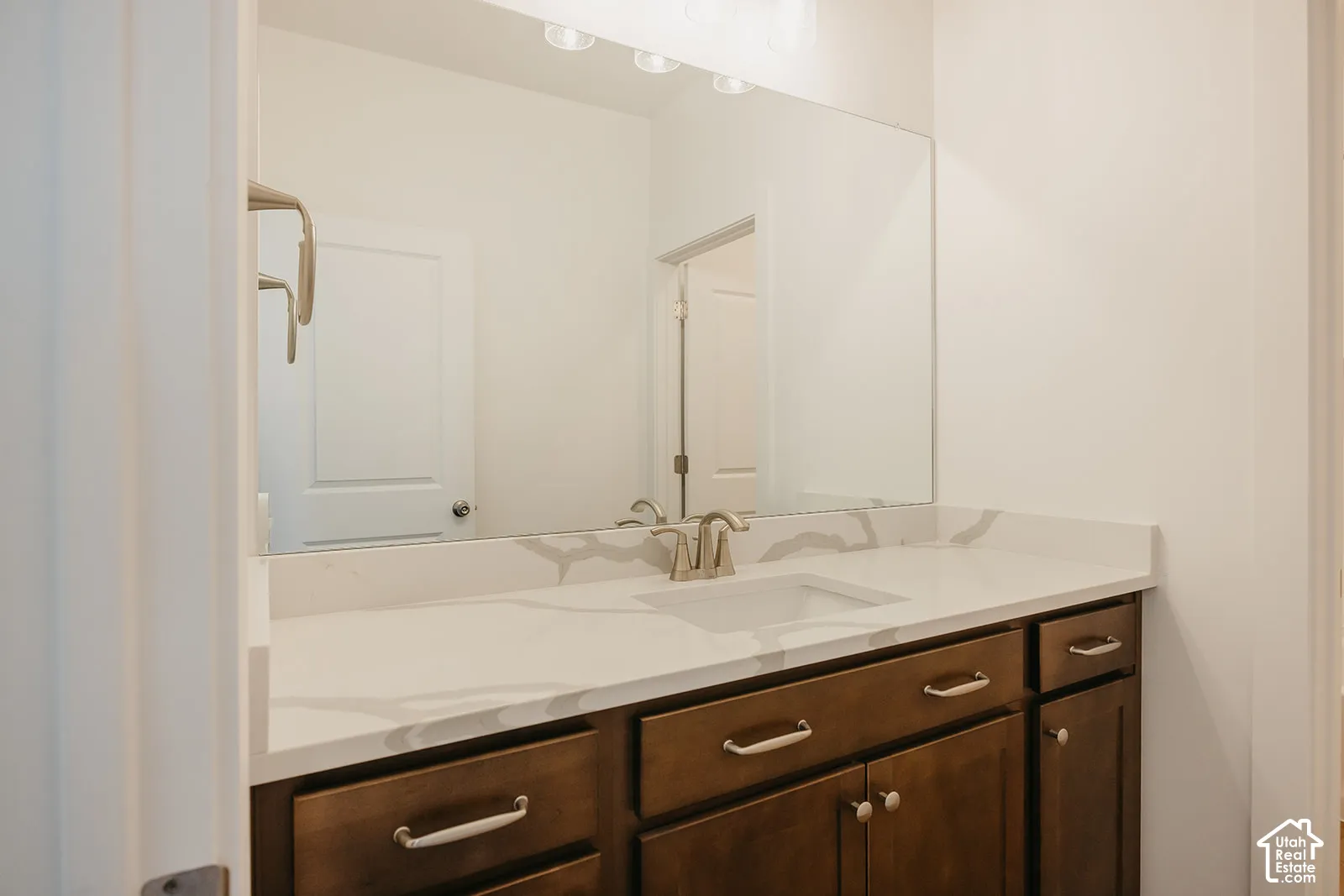 Vanity featuring dark wood-finish cabinetry, a white quartz countertop with integrated rectangular basin, chrome faucet, and a large wall-mounted mirror with multi-bulb overhead lighting