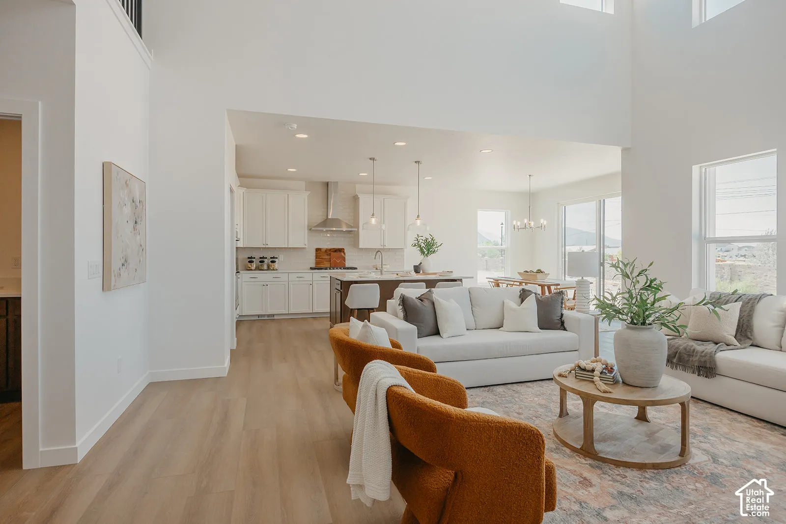 Open-concept interior featuring double-height ceilings, wood-finish flooring, recessed lighting, white cabinetry, and a kitchen island