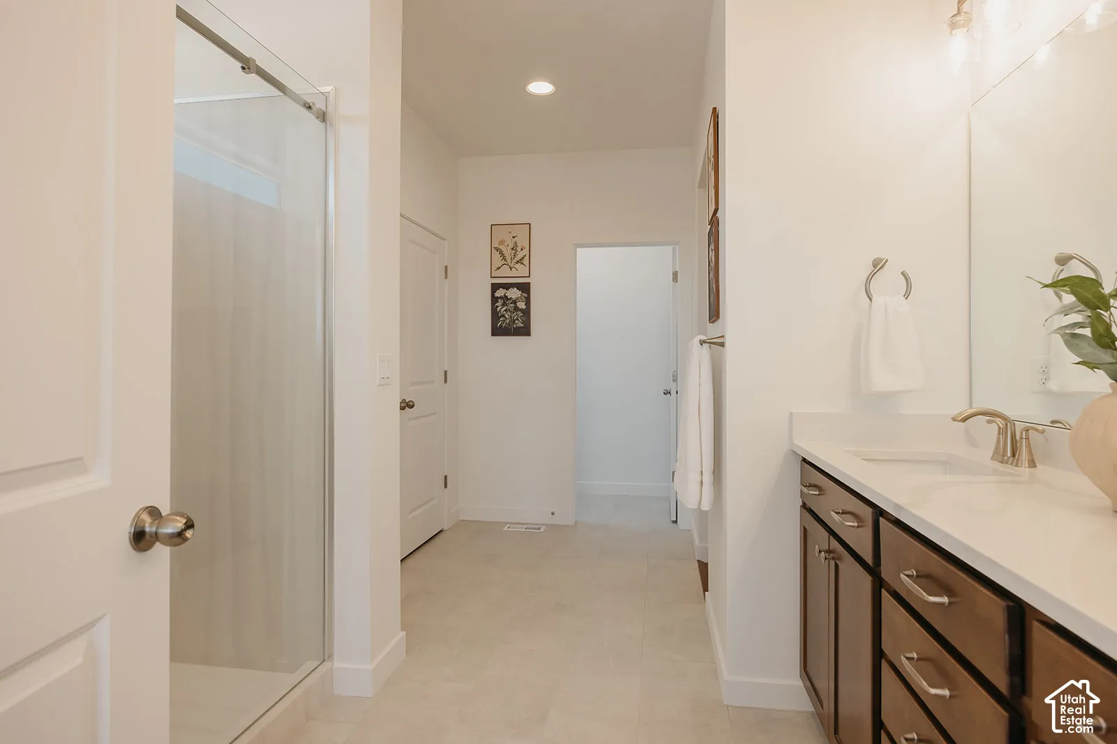 Bathroom featuring a vanity with wood-finish cabinetry, light-toned stone-style countertop, dual integrated sinks, and a glass-enclosed shower with tile surround