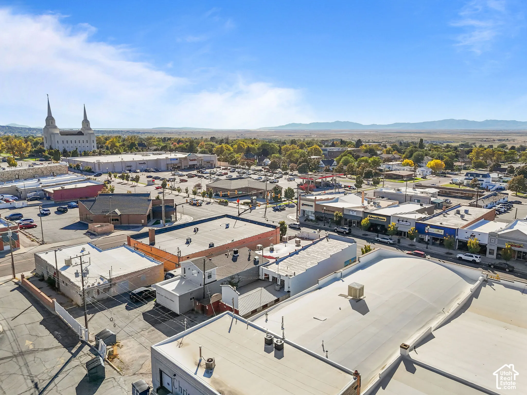 Aerial perspective of a commercial property featuring multiple flat-roof structures, proximity to paved surface parking, and mountainous horizon
