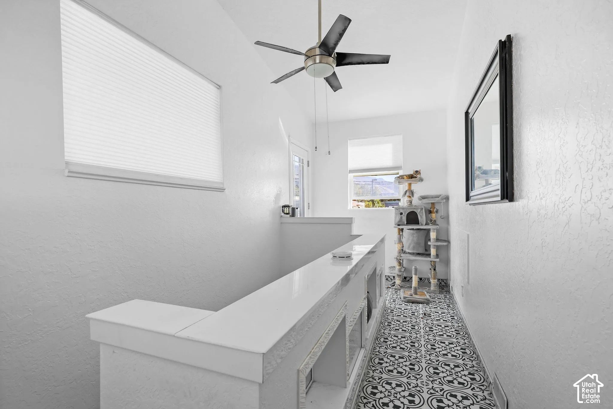 Hallway featuring patterned tile flooring, a half-wall with a smooth surface finish, a multi-blade ceiling fan, and window shades