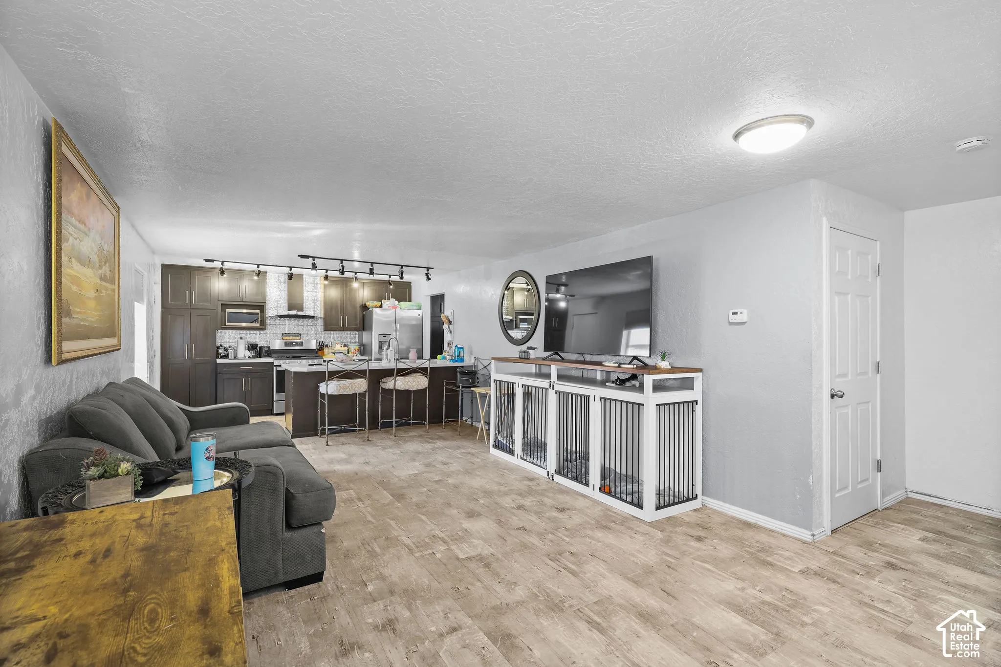 Open-concept area featuring wood-finish flooring, dark-toned cabinetry, a stone-tile backsplash, a kitchen island with bar seating, and track lighting