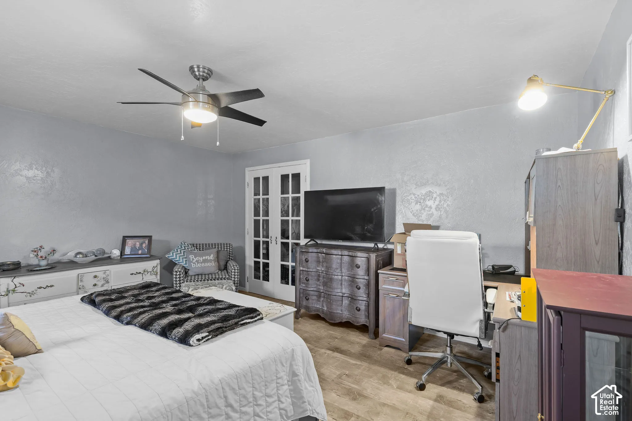 Room featuring wood-finish flooring, a multi-blade ceiling fan with integrated lighting, and glass-paned double doors