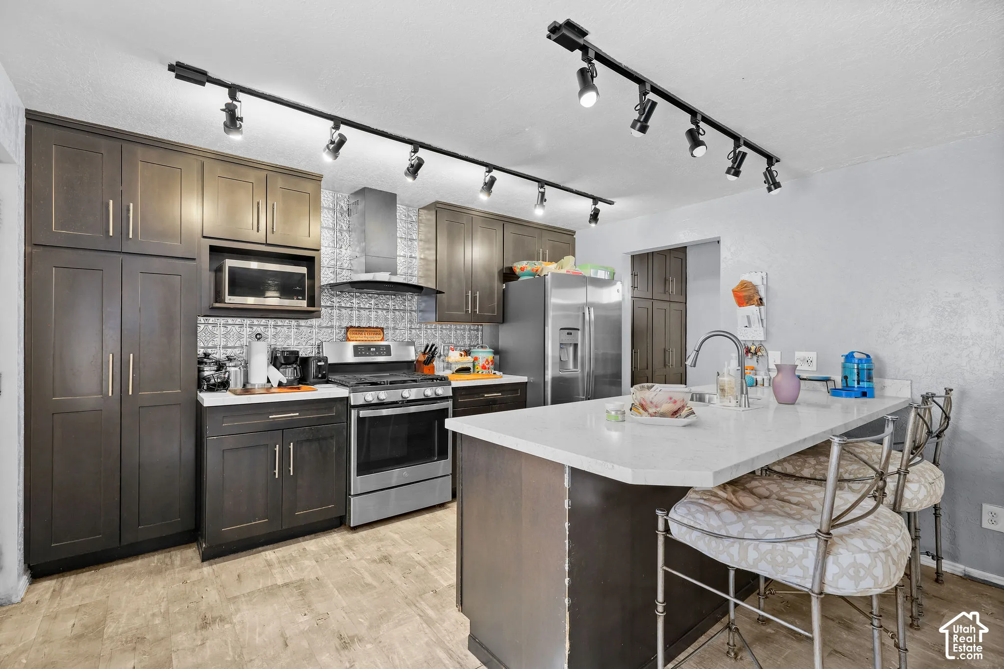 Kitchen featuring dark cabinetry, stone-finish countertops, stainless steel appliances, a patterned tile backsplash, and adjustable track lighting