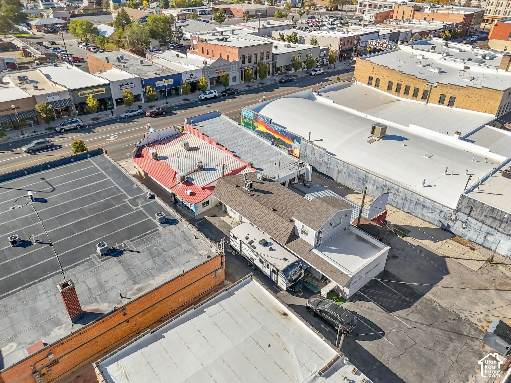 Aerial perspective of urban property featuring a pitched shingle roof, flat roofing sections, and onsite parking
