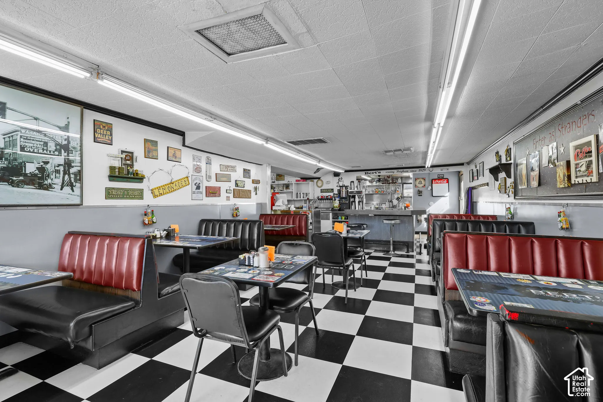 Commercial interior space featuring checkered flooring, recessed ceiling lighting, fixed vinyl booth and table seating, and a service counter