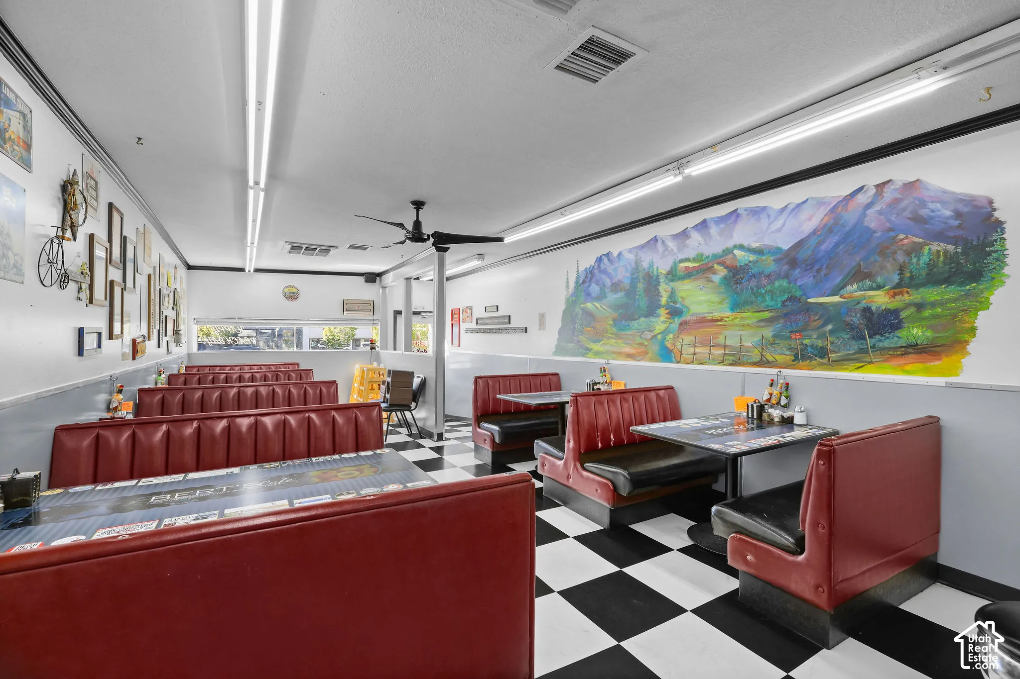 Spacious interior featuring high-contrast checkerboard flooring, integrated booth seating, linear fluorescent lighting, a ceiling-mounted fan, and a large-scale wall mural