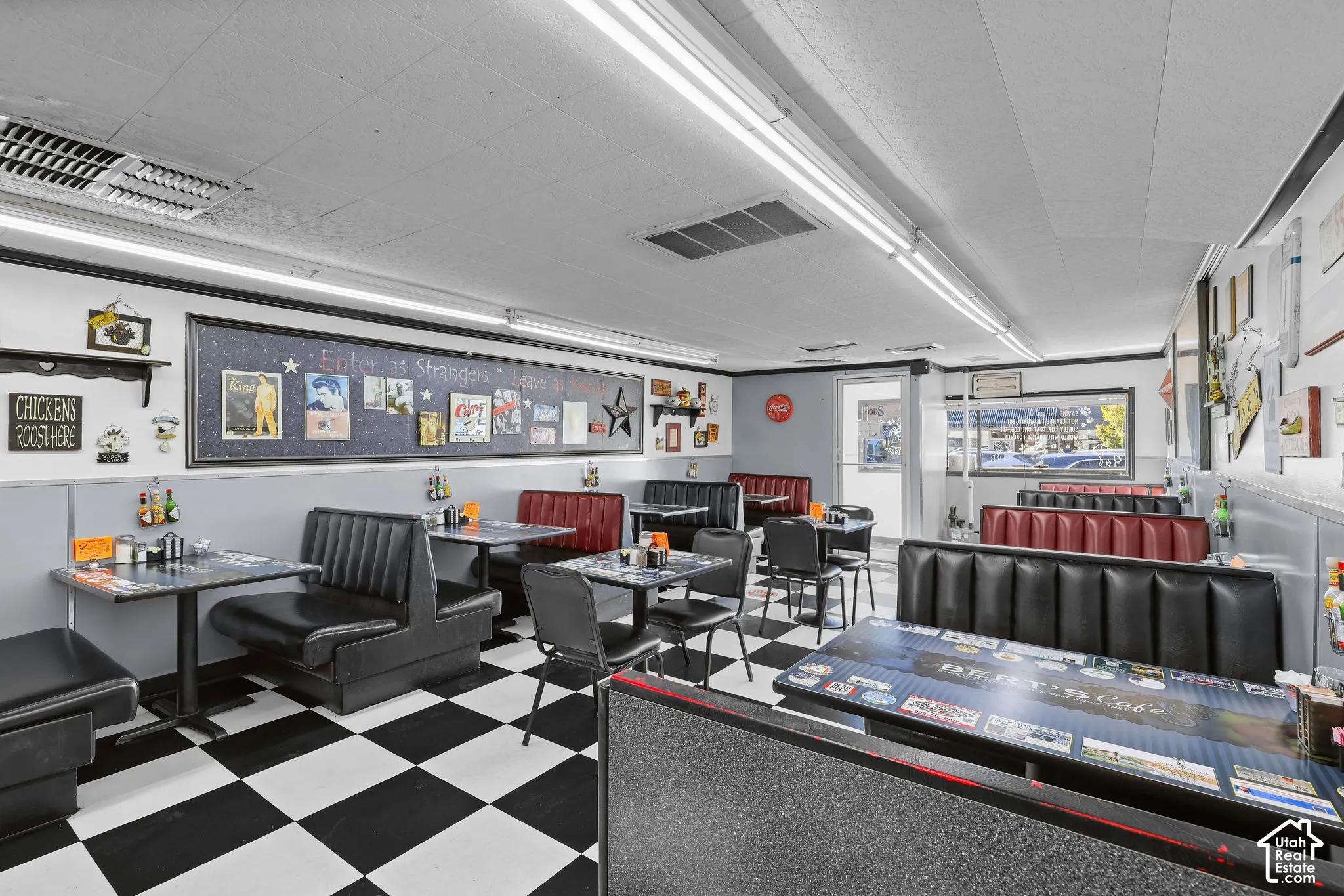 Commercial dining space featuring black and white checkerboard flooring, wall-mounted acoustic ceiling panels, linear fluorescent lighting, and built-in booth seating