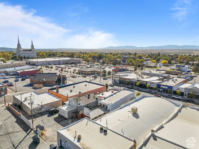 Aerial perspective of a commercial property featuring multiple flat-roof structures, proximity to paved surface parking, and mountainous horizon