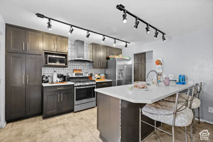 Kitchen featuring dark cabinetry, stone-finish countertops, stainless steel appliances, a patterned tile backsplash, and adjustable track lighting