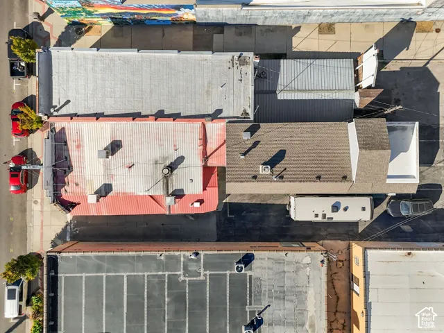 Aerial perspective of commercial property featuring a metal roof system, asphalt shingle roofing, integrated HVAC units, and paved exterior space