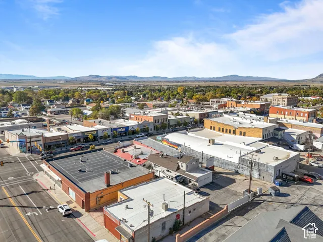 Aerial perspective of a central business district featuring street-level retail frontage, multi-parcel flat roofing systems, asphalt paved lots, and a distant mountain range backdrop