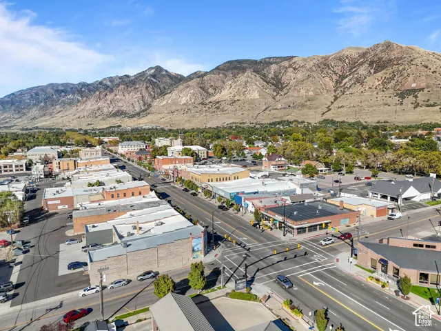 Aerial perspective of a central business district featuring diverse commercial storefronts, paved street infrastructure, and a prominent mountain range backdrop