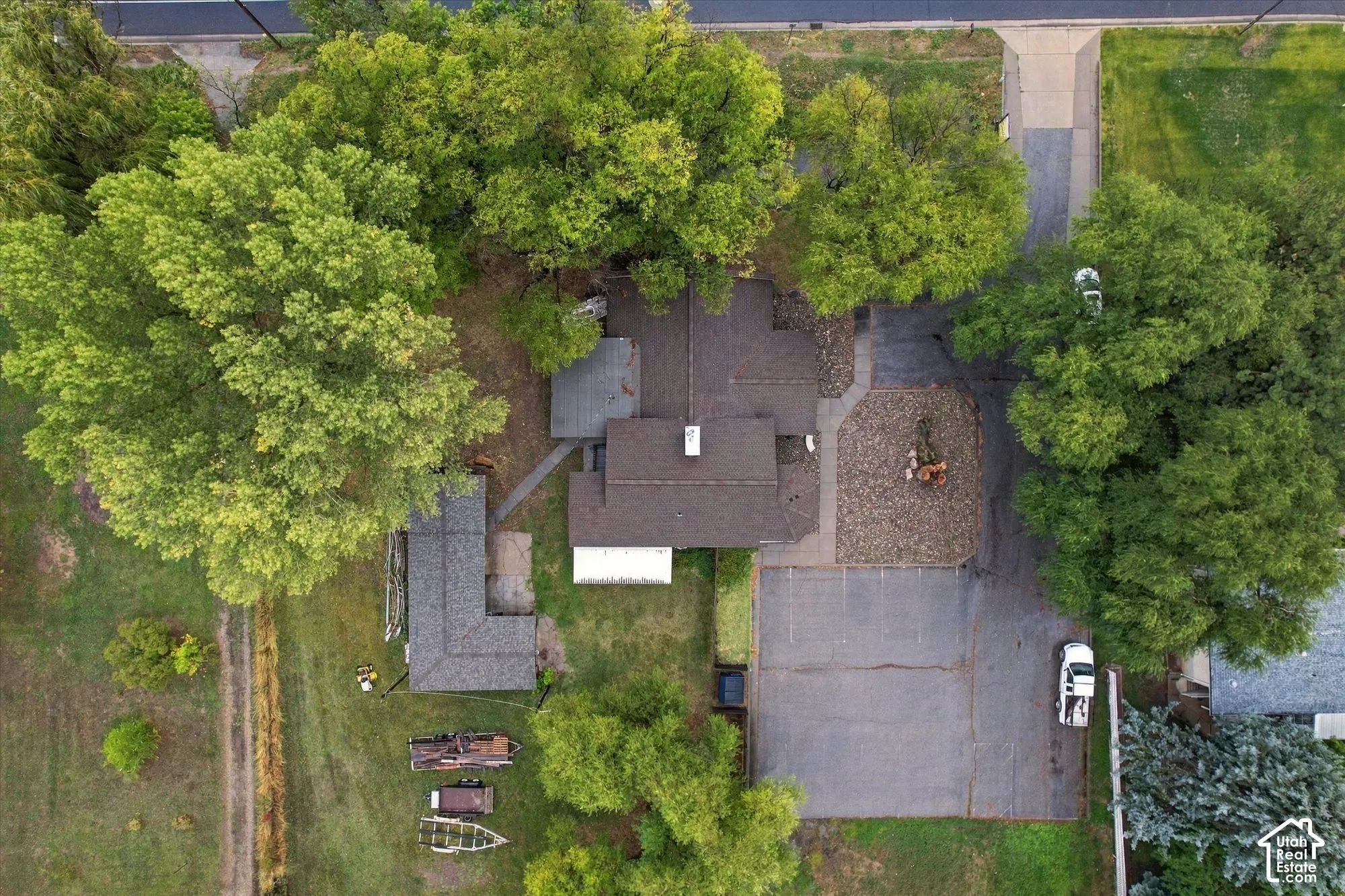 Aerial perspective of property featuring mature tree canopy, extensive asphalt driveway, aggregate surfacing, and multiple structure footprints