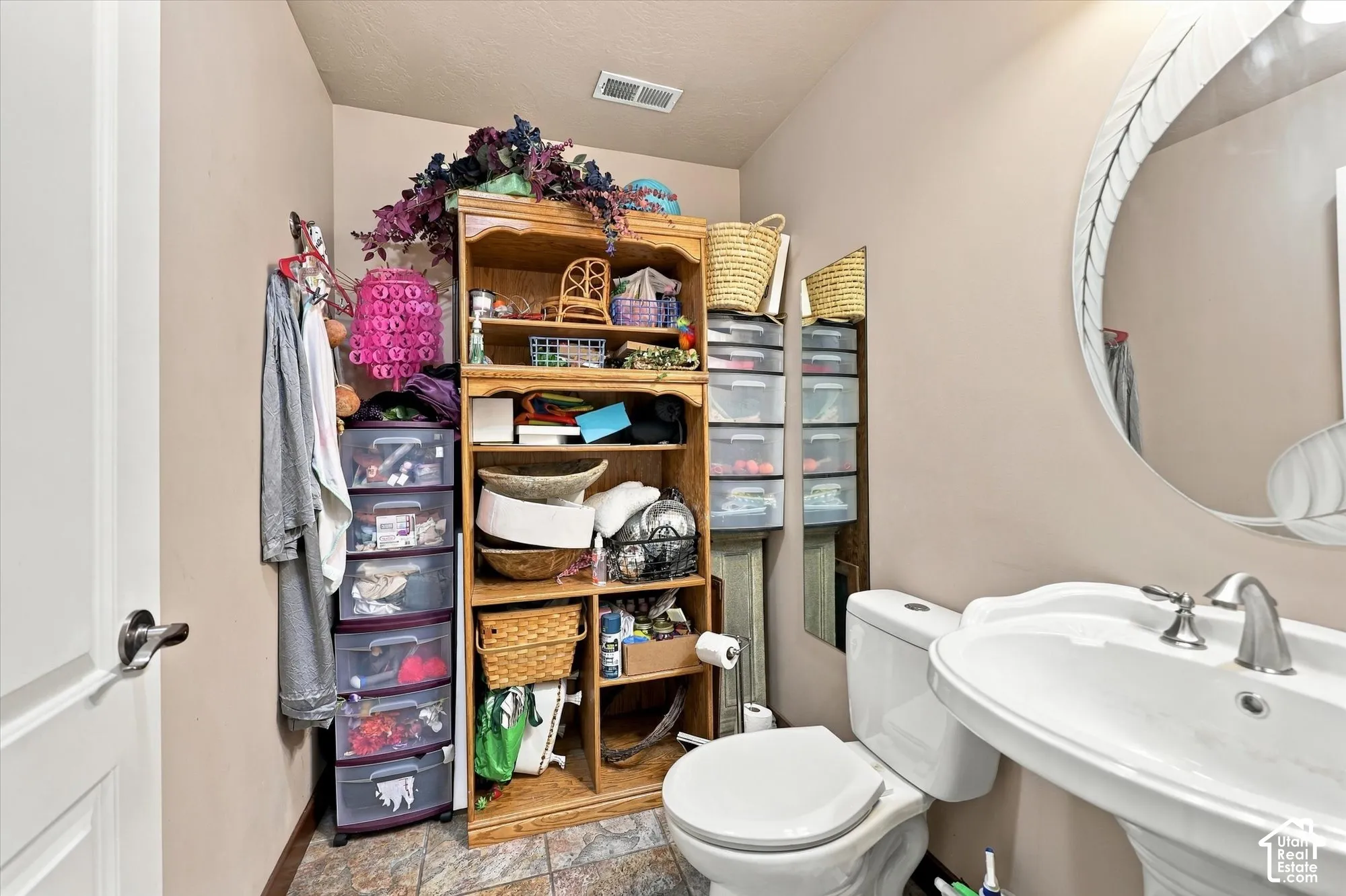Pedestal sink with polished metal faucet, round mirror, and tile flooring