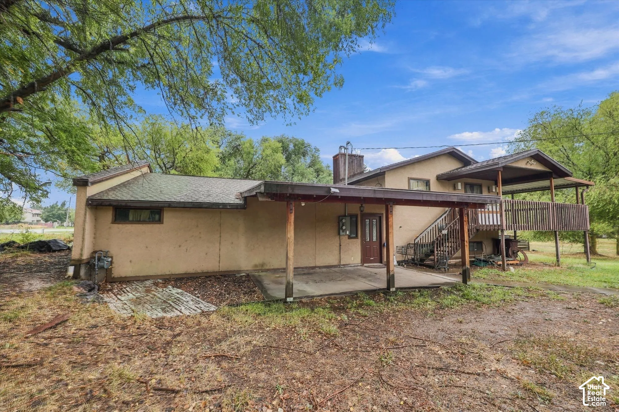 Exterior featuring a concrete patio, a covered wooden deck with railing, and a chimney