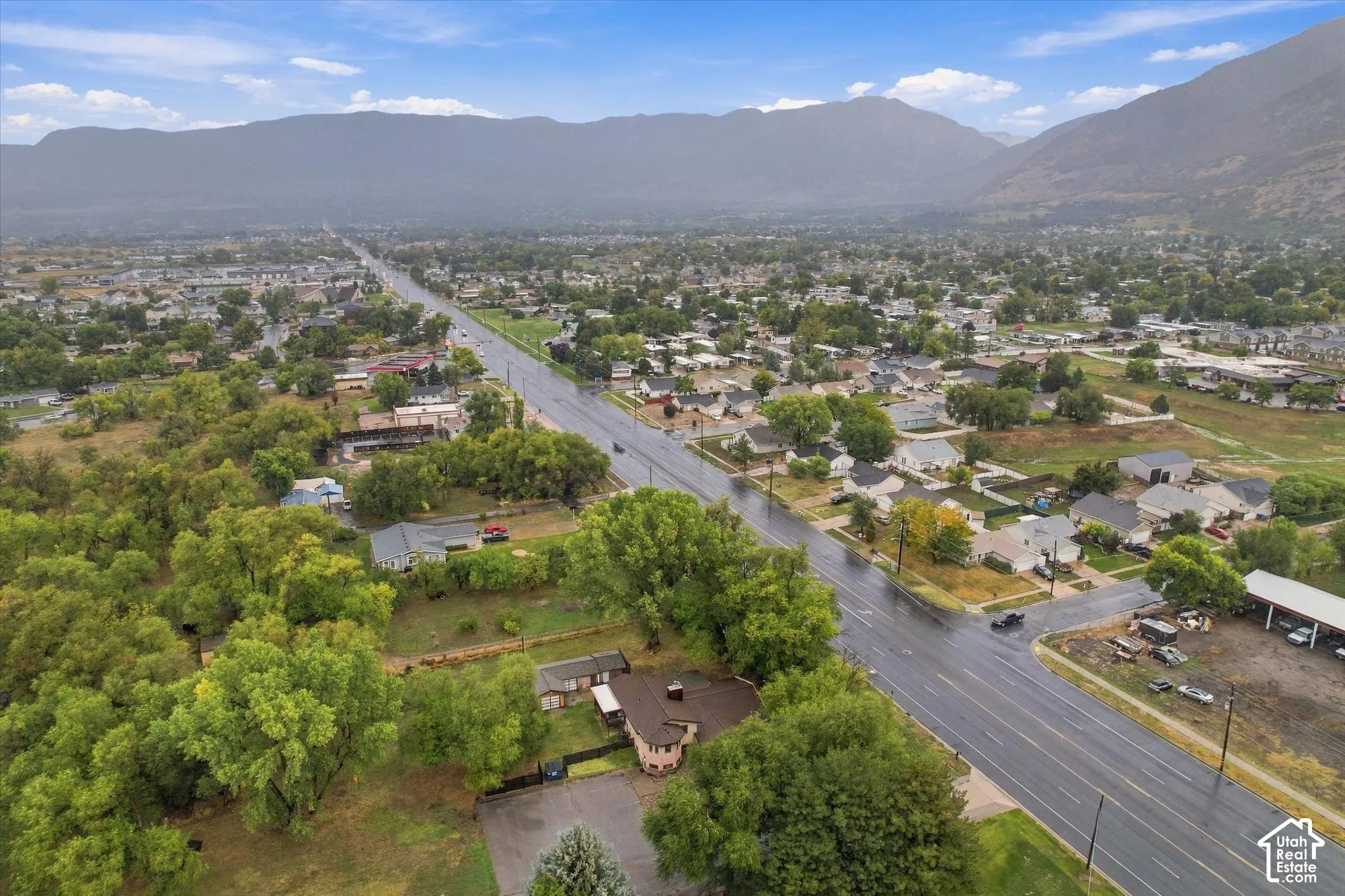 Aerial perspective featuring expansive mountain range backdrop, mature trees, and paved driveway access